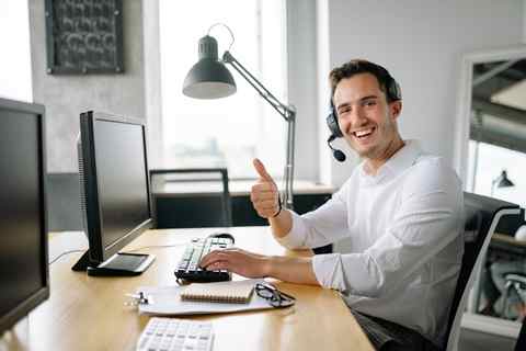 Mann im Callcenter mit Headset, lächelnd und Daumen hoch.