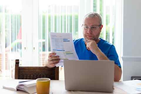 Mann arbeitet mit Laptop und Dokumenten an einem Tisch, helles Büro.